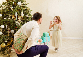 Dad hides behind his back a box with a gift for the baby daughter. 