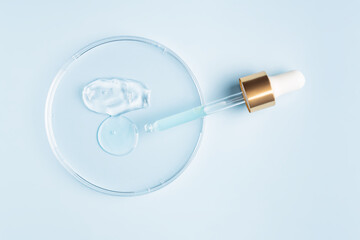 smear of cosmetic gel stroke and round transparent drop of serum in a petri dish on a blue...