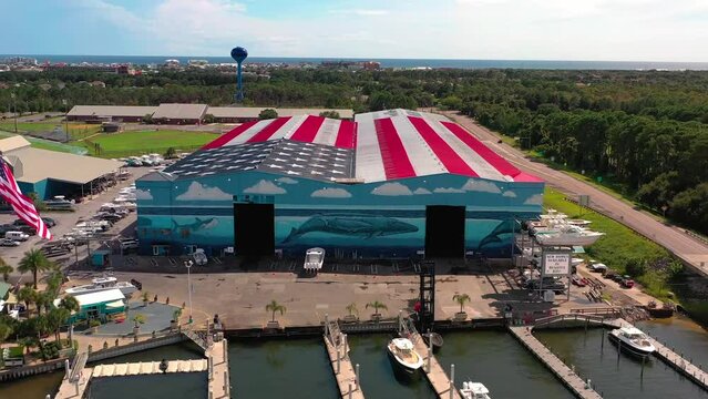 Drone view flying away from Legendary Marine in Destin Florida with the roof painted as an American Flag and it says God Bless America. You can also see the midbay bridge and Lulu's restaurant.