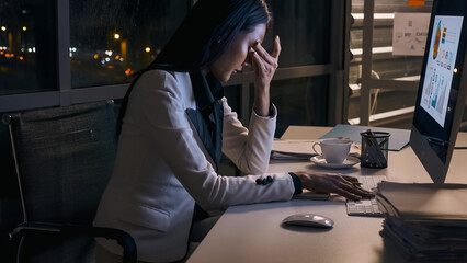 Stressed young Asian businesswoman working overtime at the office. - obrazy, fototapety, plakaty