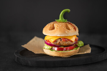 Halloween burger in a shape of pumpkin head jack o lantern on black. Scary cheeseburger on halloween party.