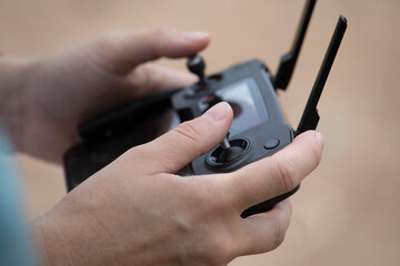 Close up of young woman's elegant hands on drone remote controller against a neutral and out of focus background.