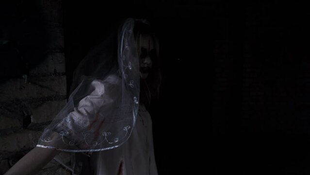Halloween. The corpse of the bride. A woman in zombie makeup and a wedding dress walks through the dark corridors of an abandoned building looking into the camera. Concept of horror, dead and zombies.