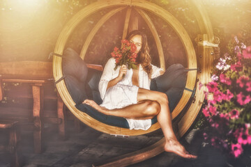 Fototapeta na wymiar beautiful woman sits on a wooden swing with a bouquet of red roses in her hand.