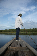 Early morning boat ride along a lake in the Mekong delta, Vietnam. A farmer is standing and paddling the boat.