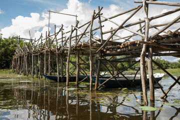Tourist canoes under wooden bridge made from mangrove wood over a canal or small river in the Mekong delta, Vietnam on a sunny day