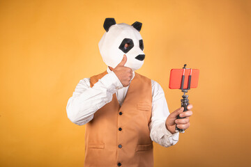 Man in panda bear mask using smartphone on a video call on a yellow background.