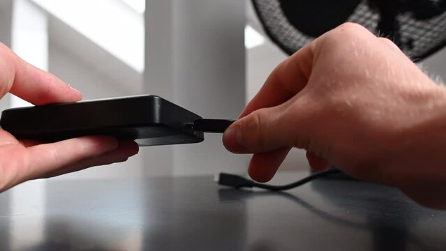 An electronice device user plugs a black cable into an external hardrive to use the storage