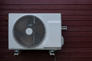 a white heat pump unit mounted on a red wood panel