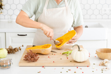 Woman hands scooping out seeds of a pumpkin with a spoon. in modern white kitchen. Cleaning process. Homemade autumn pumpkin soup recipe