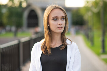 Close-up portrait of an attractive and young Caucasian girl in casual clothes in the park or on the street.