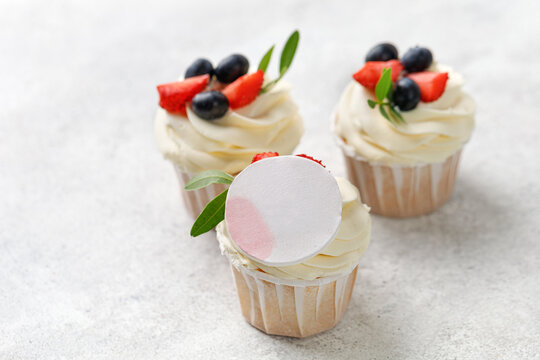 Cupcakes with fresh berries, vanilla cream, green leaves on grey background. Homemade dessert, mock up for picture.