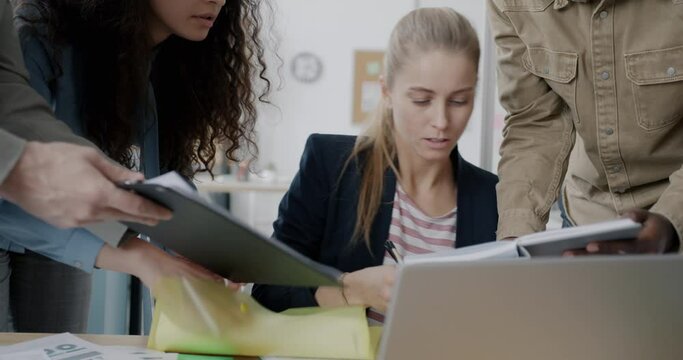 Tired young businesswoman is signing papers and talking to group of people at work. Busy employees and corporate lifestyle concept.