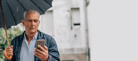 mature man with umbrella and smartphone on the street