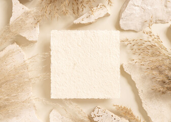 Square card near beige travertine stones and dried pampas grass top view, greeting mockup
