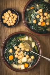 Minestrone soup with black cabbage (Toscan kale) and chickpeas in clay traditional bowls, wooden background. Italian Tuscan winter recipes. Healthy vegatarian food