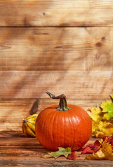 Orange pumpkin and autumn leaves on wooden background