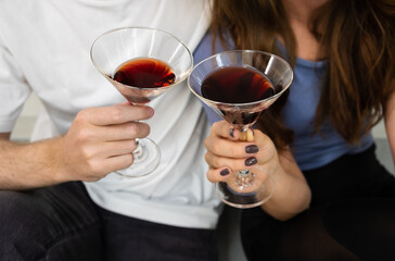 Cropped image of couple lover sitting on kitchen floor and holding glasses of cocktails or wine at home..