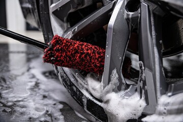 employee of a car wash or a car detailing studio carefully cleans car rims with a special brush