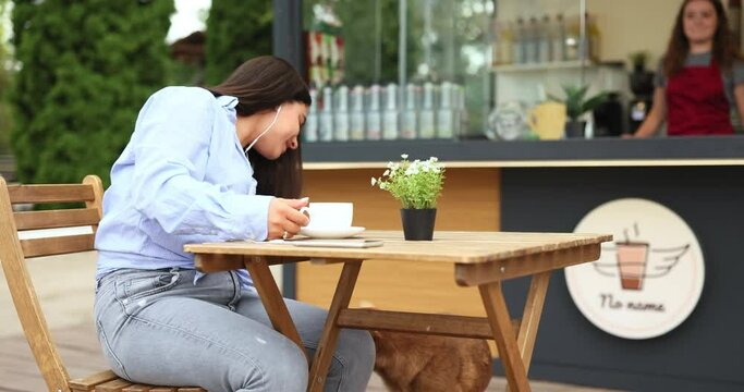 A nice woman is serving her morning coffee in front of the cafe in the street, a dog comes to her and grooms it.