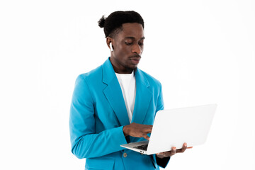 Serious african american man sitting on floor on white background in studio isolated looking at screen holding modern laptop listening to music by modern earphones.