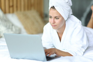 Woman on a bed after showering using laptop