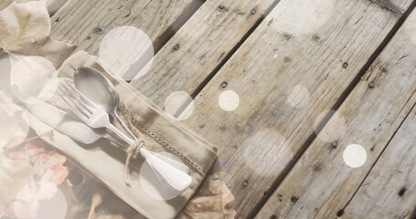Image of light spots over cutlery and leaves on wooden background