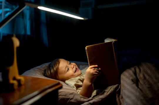Happy Boy Reading Book Lying On Bed At Home