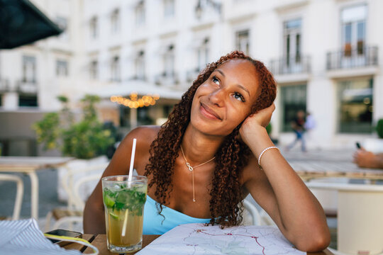 Thoughtful woman with glass of mojito and map sitting at sidewalk cafe