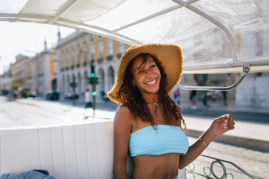Cheerful young woman wearing hat taking tuk tuk ride on sunny day