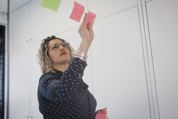 Mature businesswoman sticking adhesive notes at office