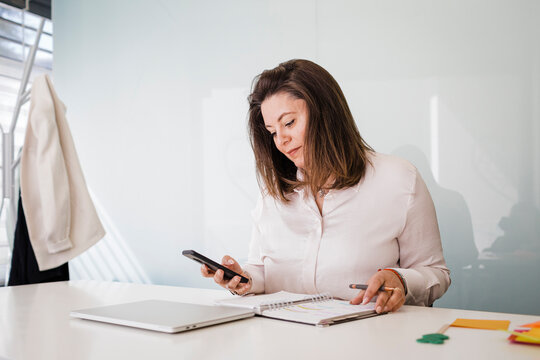 Mature businesswoman using smart phone at desk in office