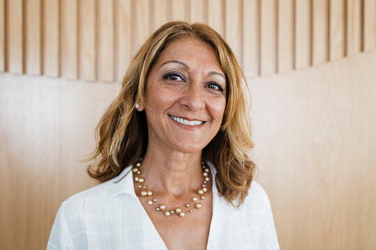 Happy mature businesswoman with blond hair in front of wall