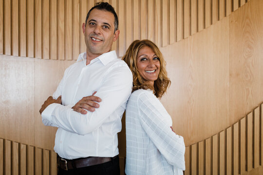 Happy business colleagues with arms crossed standing in front of wall
