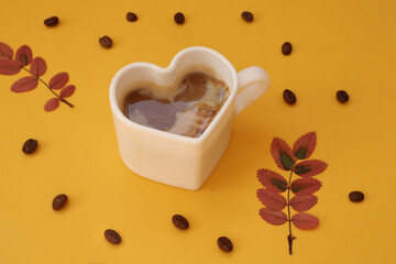  Good autumn morning wishes: heart-shaped coffee mug, close-up, colorful autumn leaves, coffee beans on a yellow background, side view