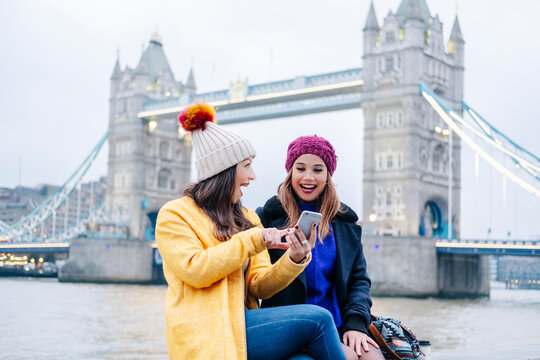 London, United KingdomTwo girls using smartphone in front of Tower Bridge