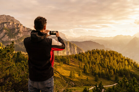Man photographing mountain through smart phone at sunset