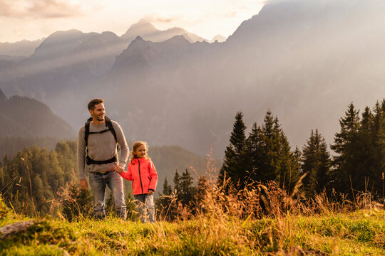 Smiling man holding daughter's hand hiking on mountain