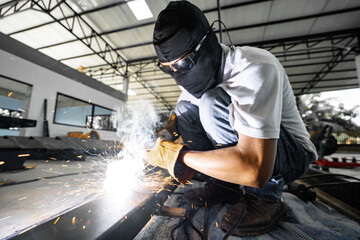 Picture of an Asian welder welding a steel structure in a factory building.