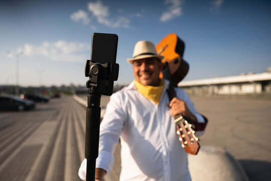 Smiling guitarist holding guitar taking selfie through mobile phone on tripod
