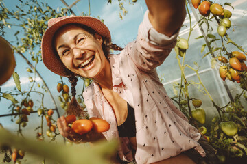 Cheerful farmer holding fresh tomatoes in greenhouse