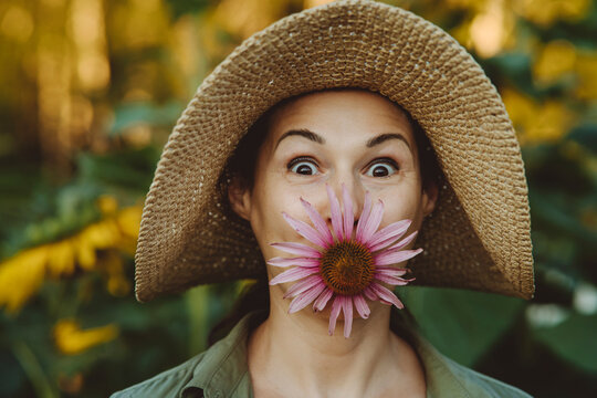 Mature woman with hat carrying pink flower in mouth