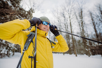 Senior man putting on snow glasses, preparing for ride in snowy forest.