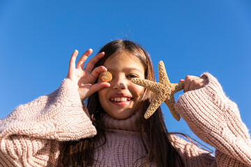 Girl with shell and starfish in front of blue sky