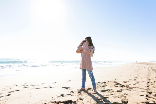 Girl standing with camera taking photos at beach