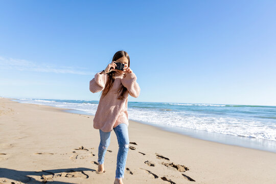 Girl running and clicking photos from camera at beach