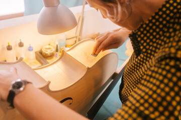 Luthier with hand tool carving on double bass musical instrument at workshop
