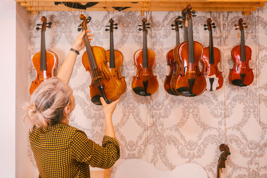 Luthier hanging violins in front of wall at store