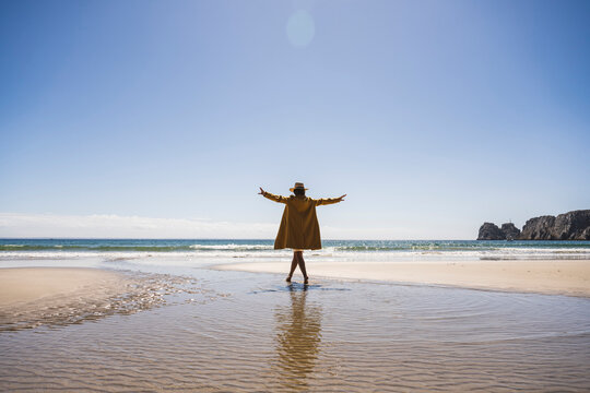 Woman with arms outstretched walking in water at beach on sunny day