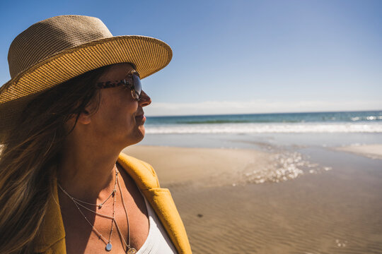 Mature woman wearing hat and sunglasses at beach on sunny day